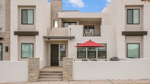 A modern two-story house with a front entrance, a red umbrella, and a stone pillar. - Pirates Den at the Shores: Desert Color Lagoon + Beaches (Saint George)