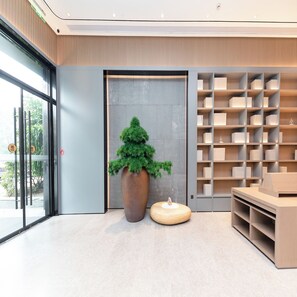 A modern interior with a large potted tree, a wooden bench, and a bookshelf. - Ji Hotel (Hangzhou)