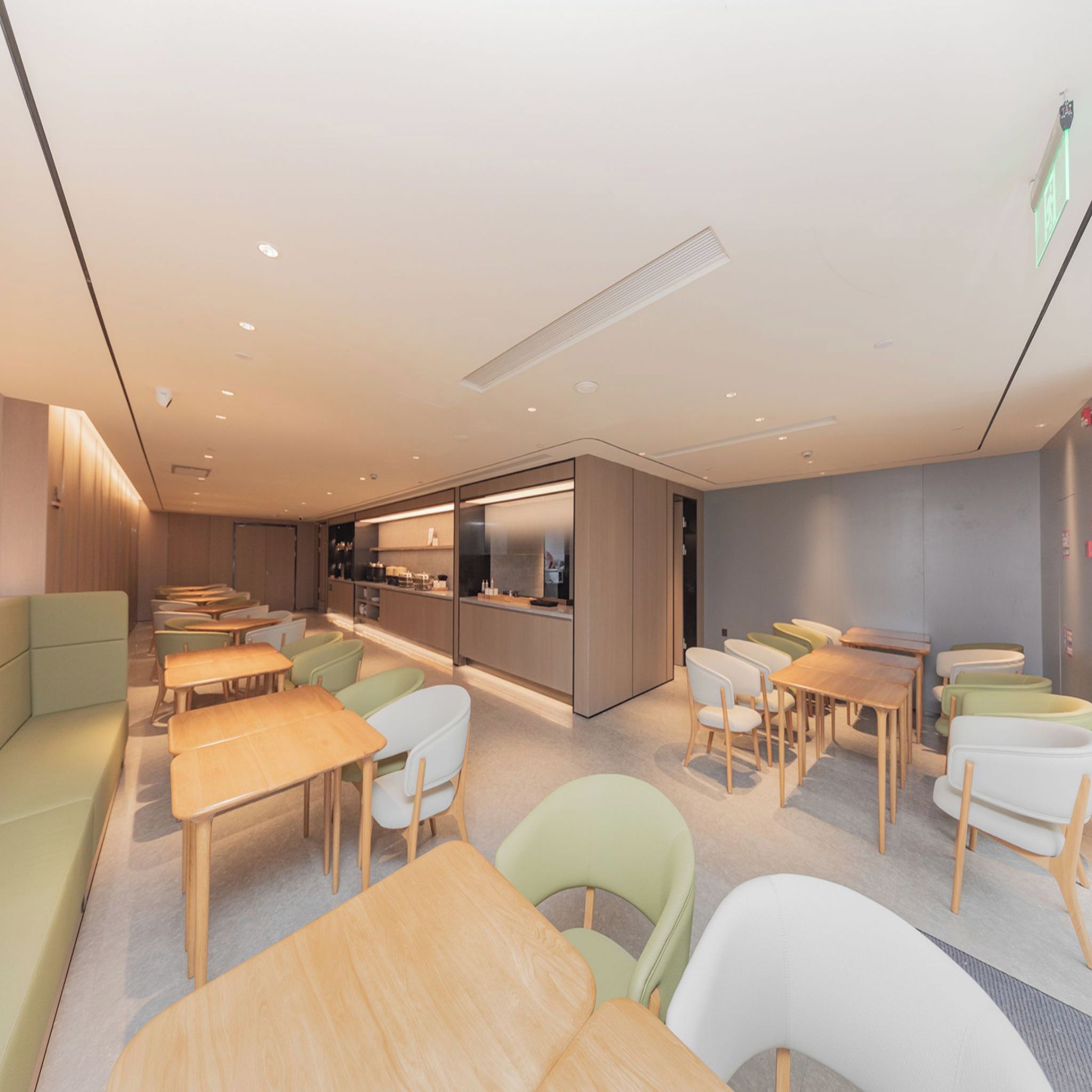 A modern dining area with wooden tables and chairs, a kitchen area, and a seating area with cushioned benches.