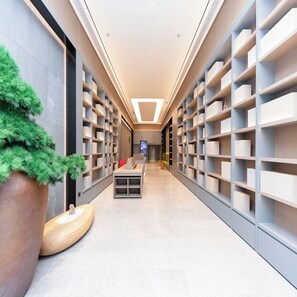 A modern library with bookshelves on both sides of a central walkway, a large potted plant, and a seating area with a television. - Ji Hotel (Hangzhou)