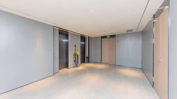 A modern hallway with a light-colored floor, a potted plant, and a green exit sign.