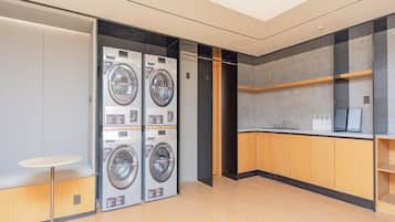 A modern laundry room with four stacked washing machines, a small round table, and wooden cabinets.
