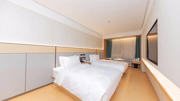 Quarto de hotel com cama grande, mesa de cabeceira, televisão e janela com cortinas.