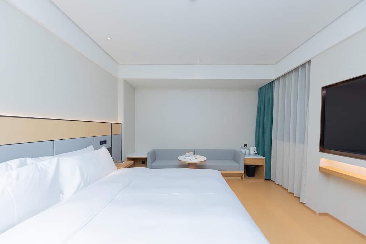 Et hotelværelse med en stor seng, en sofa, et lille bord med lampe og et fjernsyn ophængt på væggen.
