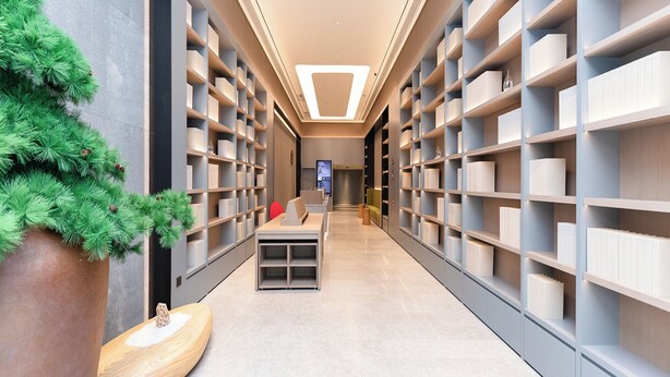 A modern library with bookshelves on both sides of a central walkway, a large potted plant, and a seating area with a television. - Ji Hotel (Hangzhou)