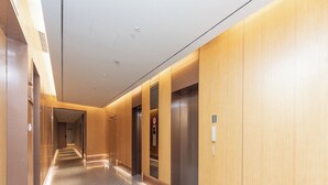 A modern hallway with a marble floor, wooden paneling on the walls, and two elevators. - Ji Hotel (Hangzhou)
