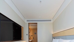 A modern hotel room with a large bed, a flat-screen TV mounted on the wall, a bedside table with a lamp, and a bathroom visible through an open door. - Ji Hotel (Hangzhou)