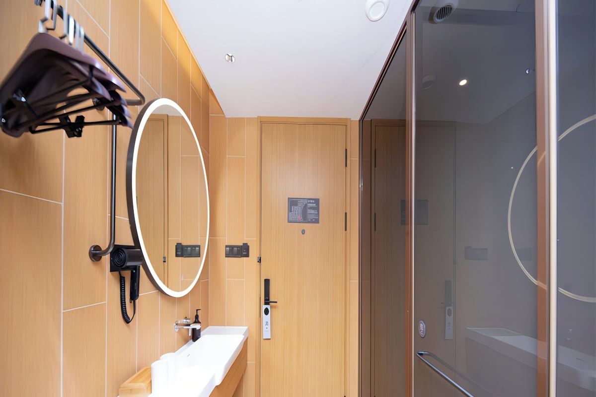 A modern bathroom with a wooden vanity, a mirror, a bench, and a glass shower enclosure.