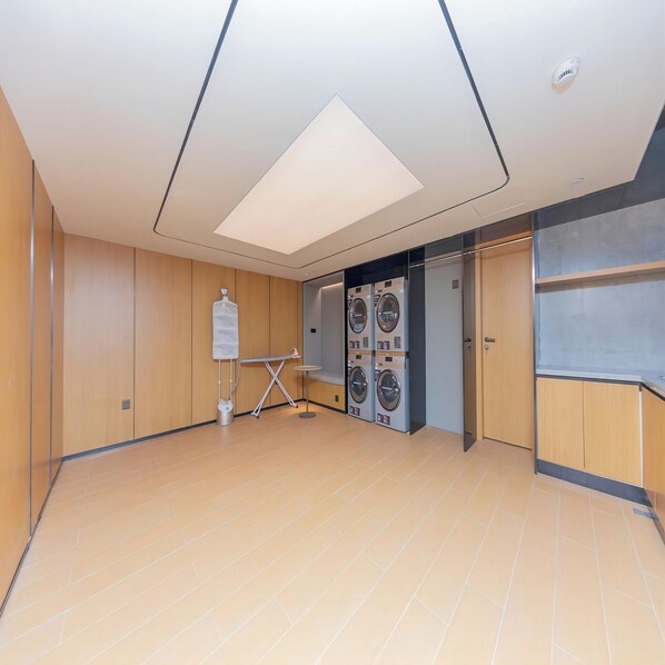 A modern room with wooden paneling, a large ceiling light, a whiteboard, and a row of washing machines. - Ji Hotel (Hangzhou)