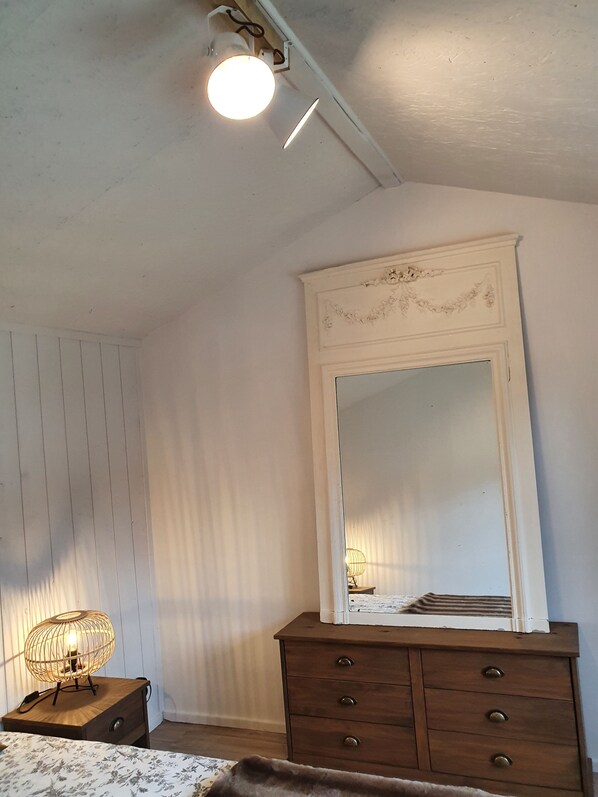 A bedroom with a wooden dresser, a mirror, and a bedside lamp.