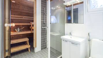 Uma casa de banho moderna com sauna de madeira, cabine de duche em vidro e lavatório branco com espelho.