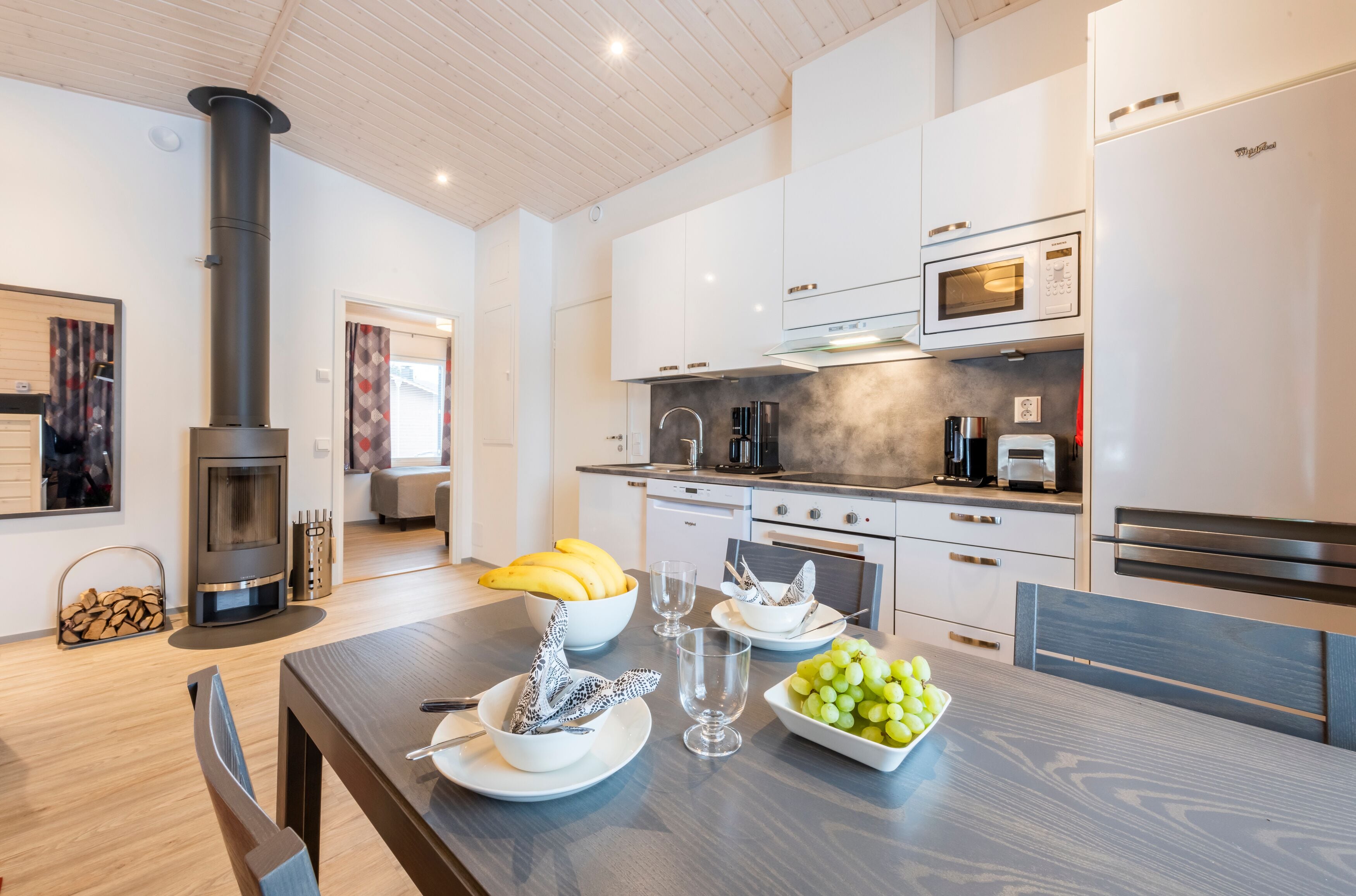 A modern kitchen with white cabinets, a black stove, and a dining area with a wooden table set for a meal.