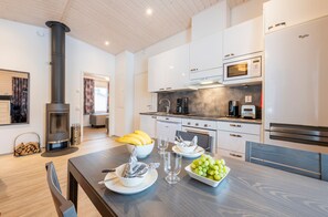 Una cocina moderna con armarios blancos, una estufa negra y un comedor con mesa de madera dispuesta para una comida.