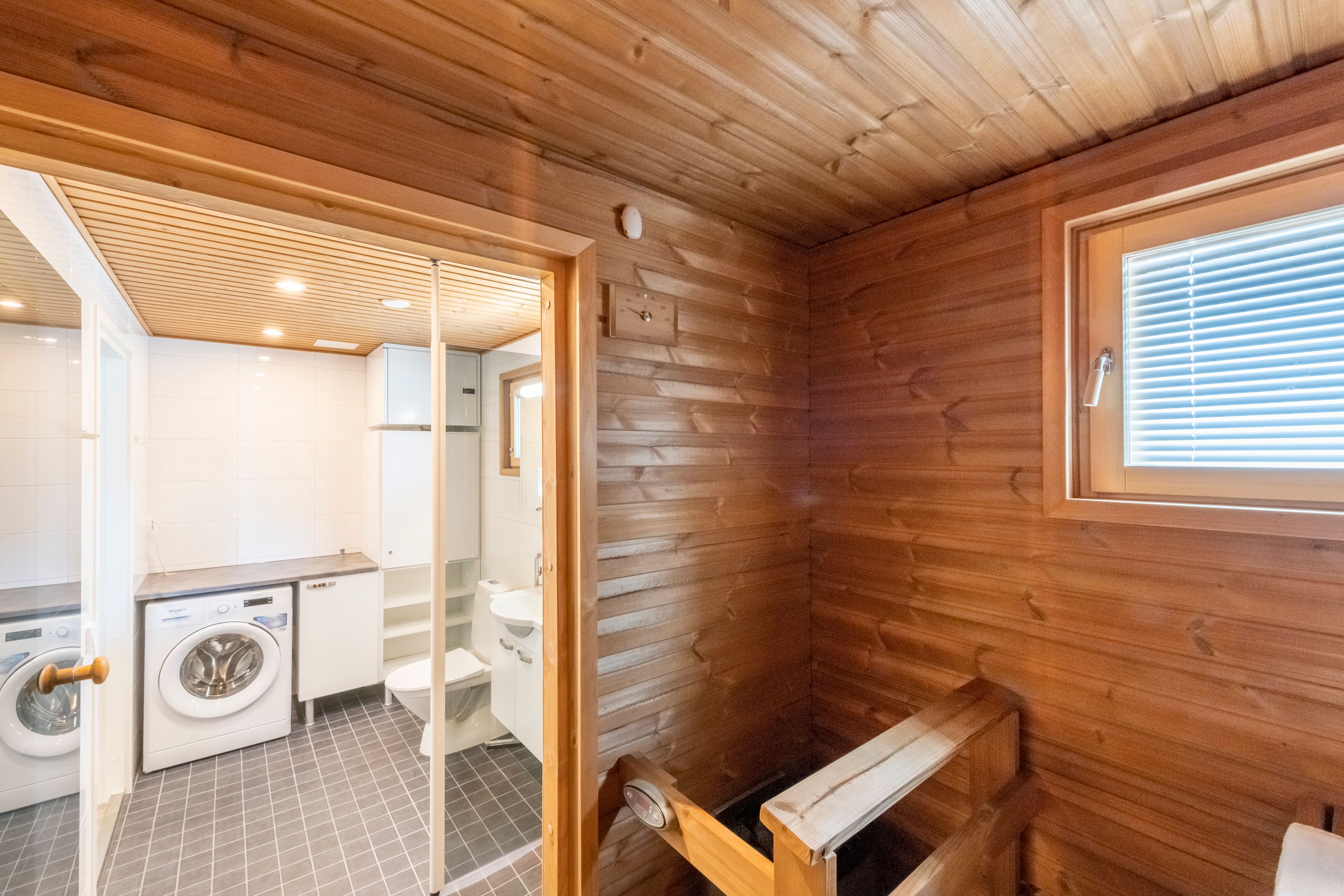 A wooden cabin interior with a washing machine, toilet, and a small window.