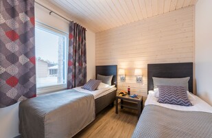 Una habitación con dos camas individuales, una mesita y una ventana con cortinas.