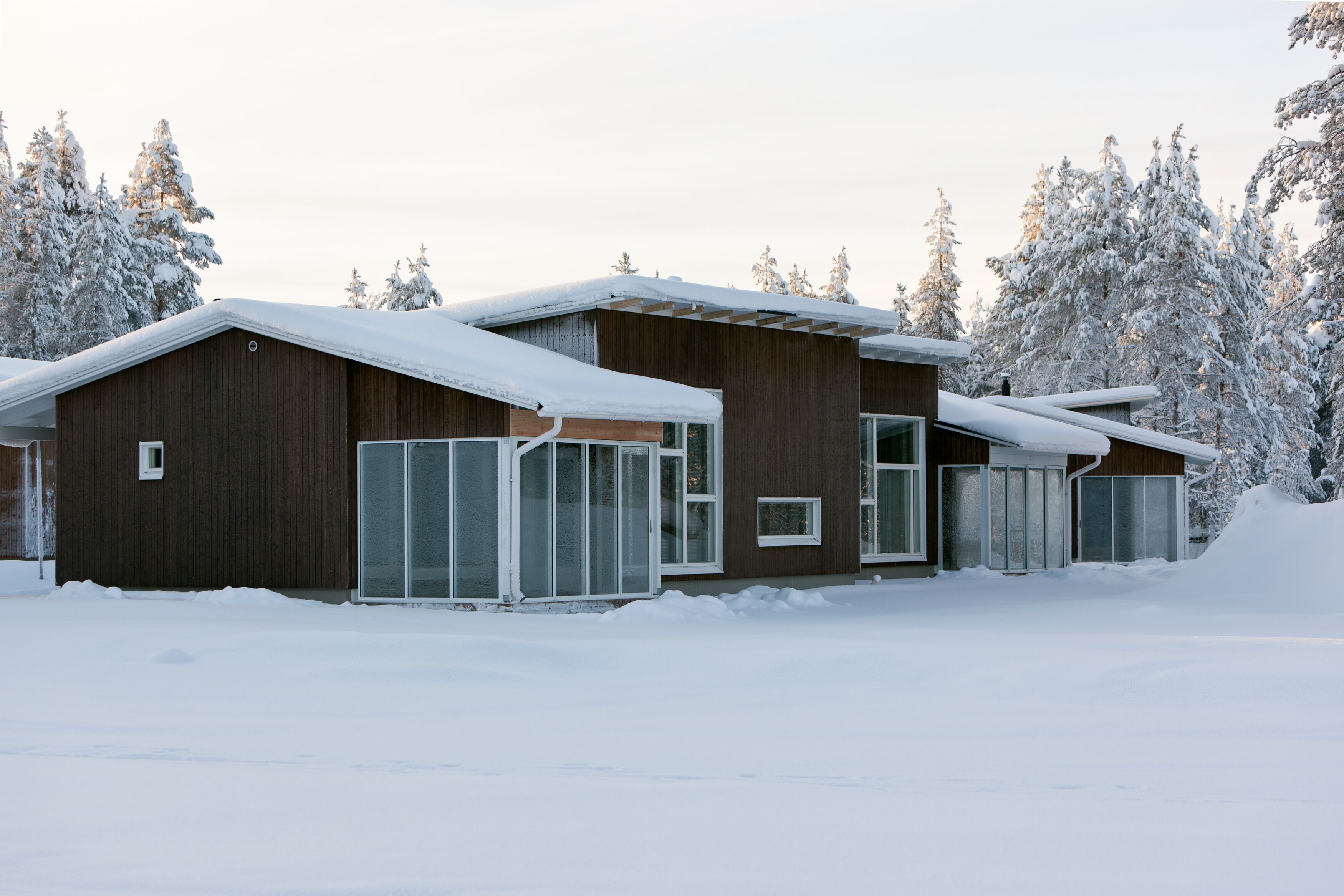 A modern building with large windows and a wooden exterior, surrounded by snow-covered trees.