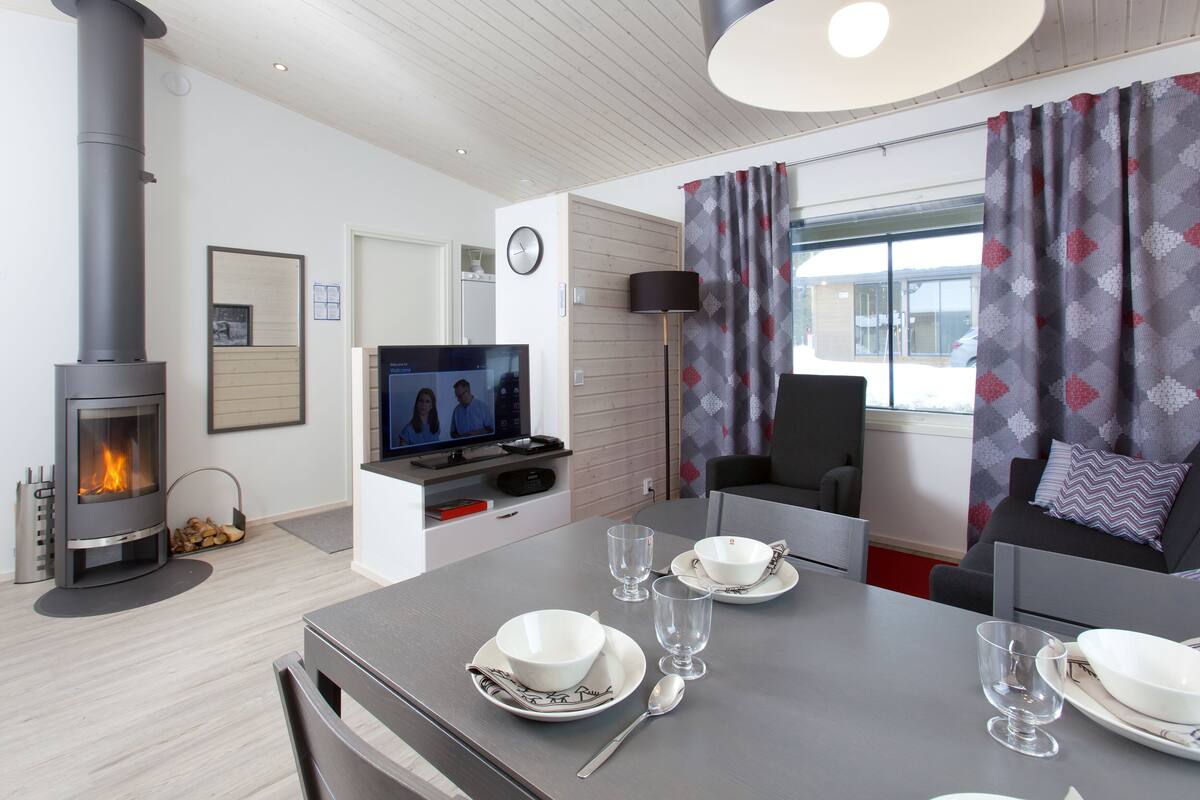 Una sala de estar moderna con una estufa de leña, una mesa de comedor con platos y vasos, un sofá y un televisor.