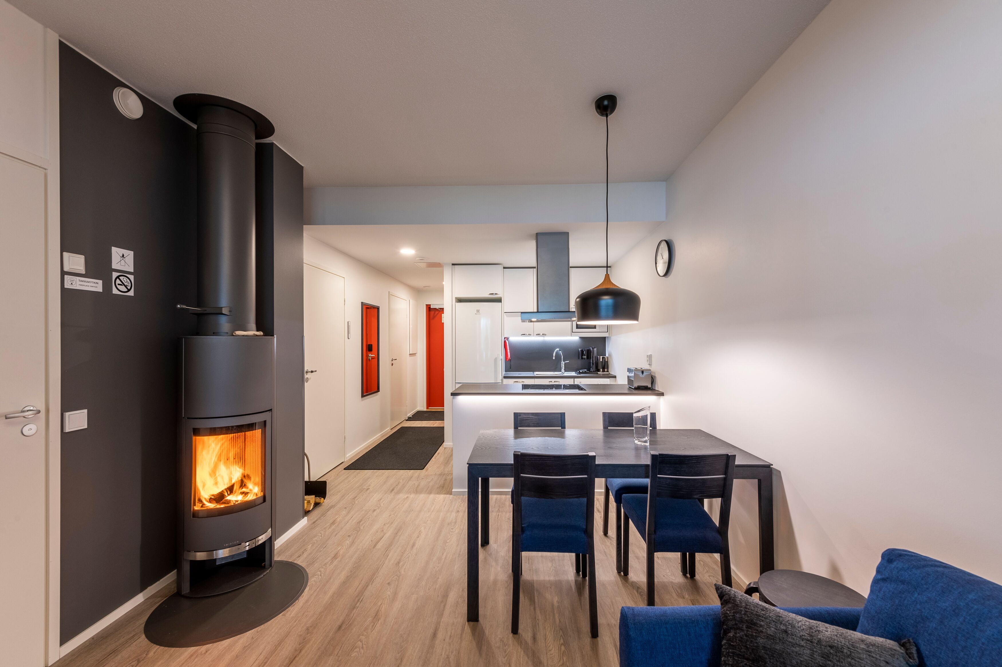 A modern kitchen with a central island, a dining area with blue chairs, and a wood-burning stove.