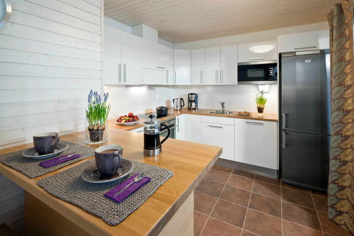 Una cocina moderna con armarios blancos, un refrigerador de acero inoxidable, un microondas y una cafetera.