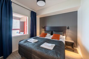 Una cama bien hecha con un cabecero oscuro, dos almohadas anaranjadas y toallas blancas dobladas.