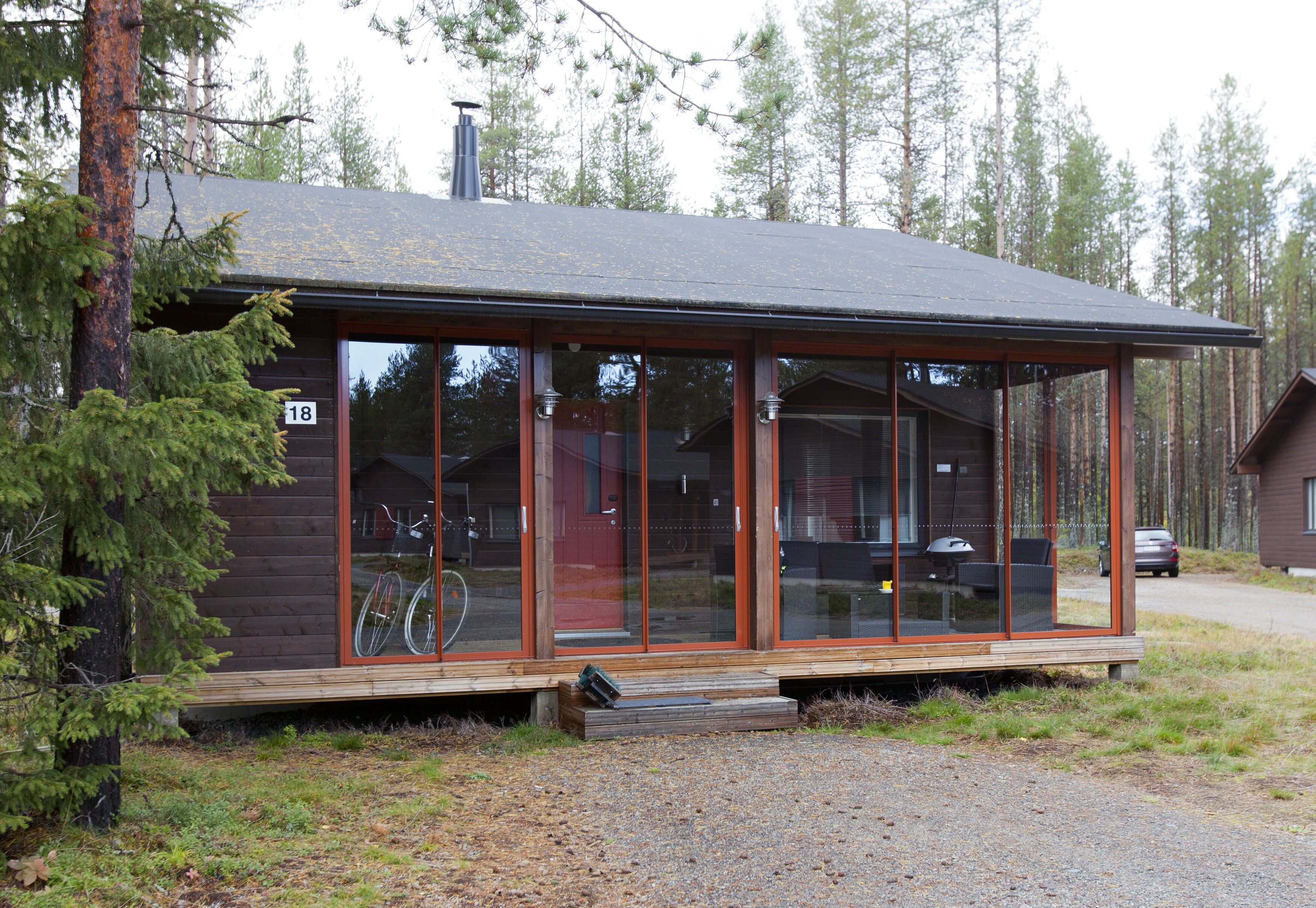 A cabin with large glass windows, a wooden deck, and a number '18' sign.