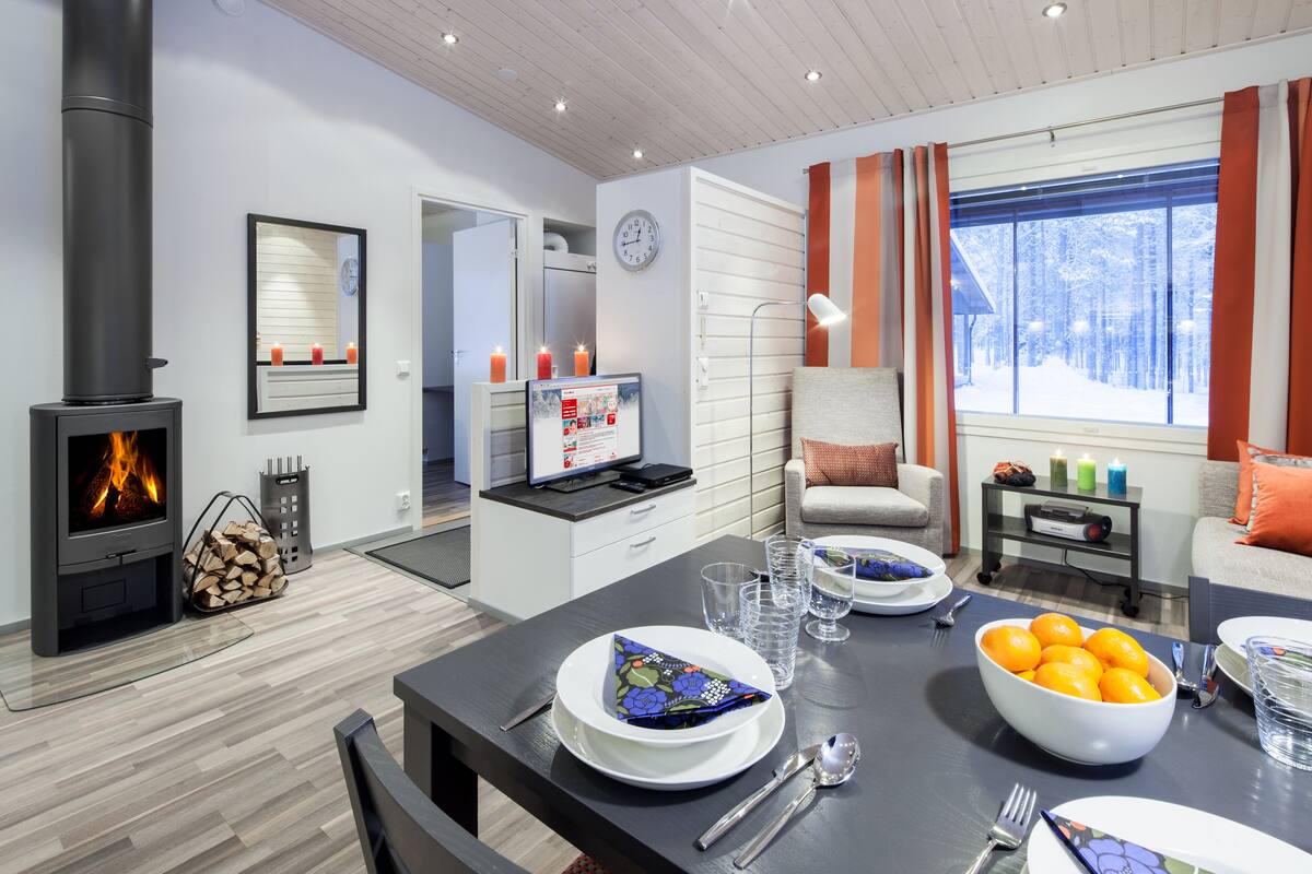 Una sala de estar moderna con chimenea, una mesa de comedor con platos y vasos, y un rincón de descanso acogedor con vista a un paisaje nevado.
