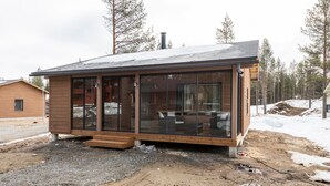 Une cabane moderne dotée de grandes fenêtres, d’un revêtement extérieur en bois et d’une allée gravillonnée.