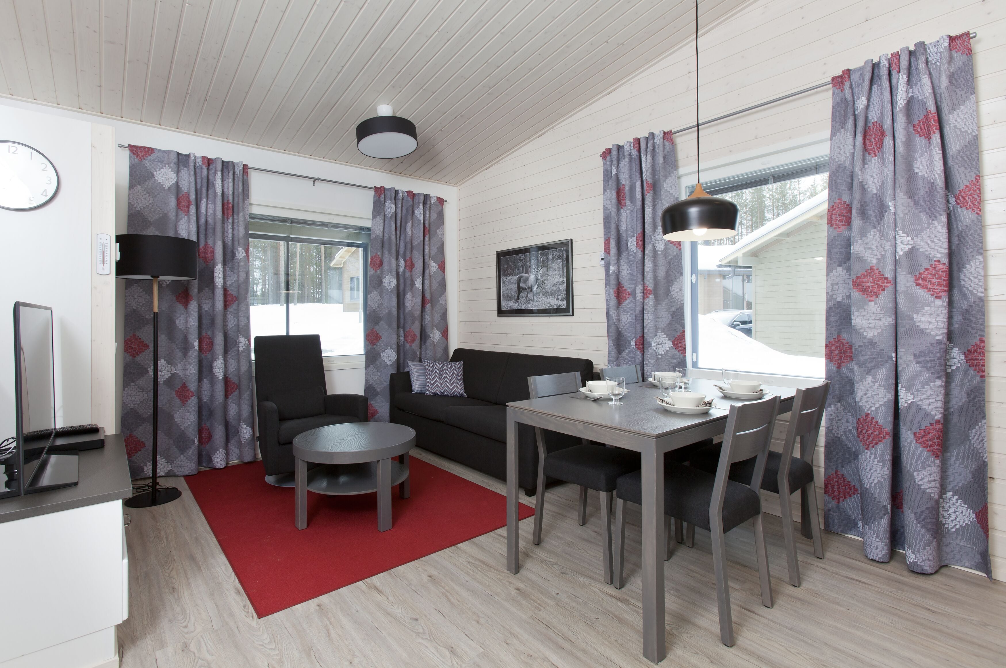 A modern living room with a sofa, dining table, and chairs, a red rug, and patterned curtains.