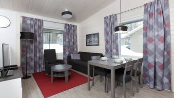 A modern living room with a sofa, dining table, and chairs, a red rug, and patterned curtains.