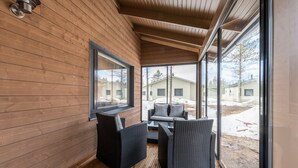 Un intérieur en bois avec une grande fenêtre, des meubles en osier noir et une vue sur un espace extérieur enneigé.