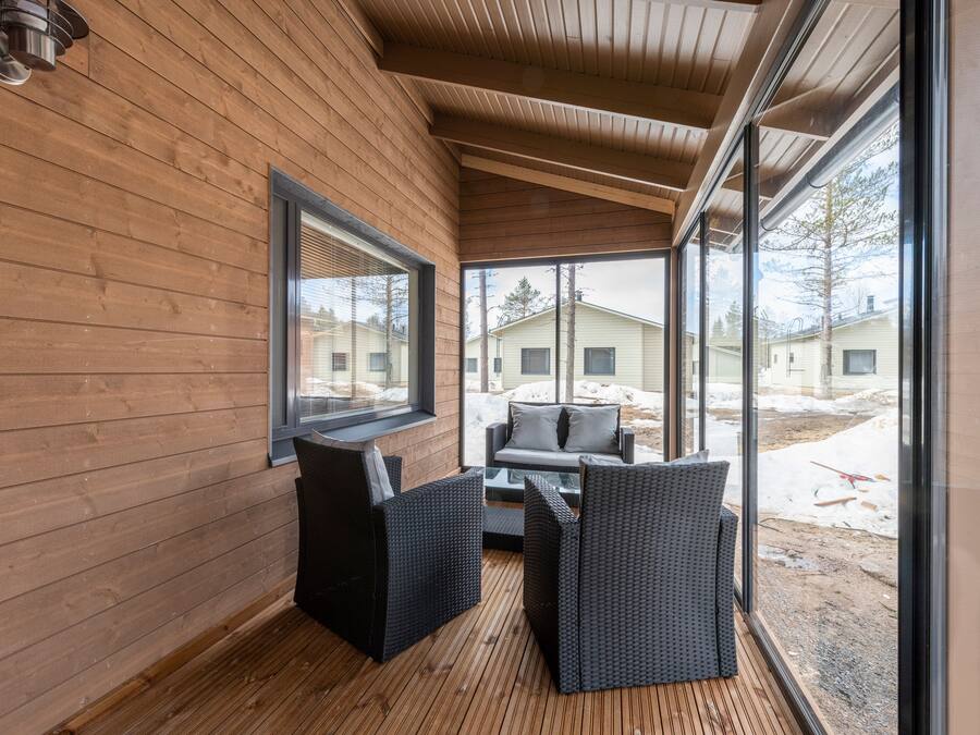 Interior de madera con un amplio ventanal, mobiliario de mimbre negro y vistas a un paisaje nevado.