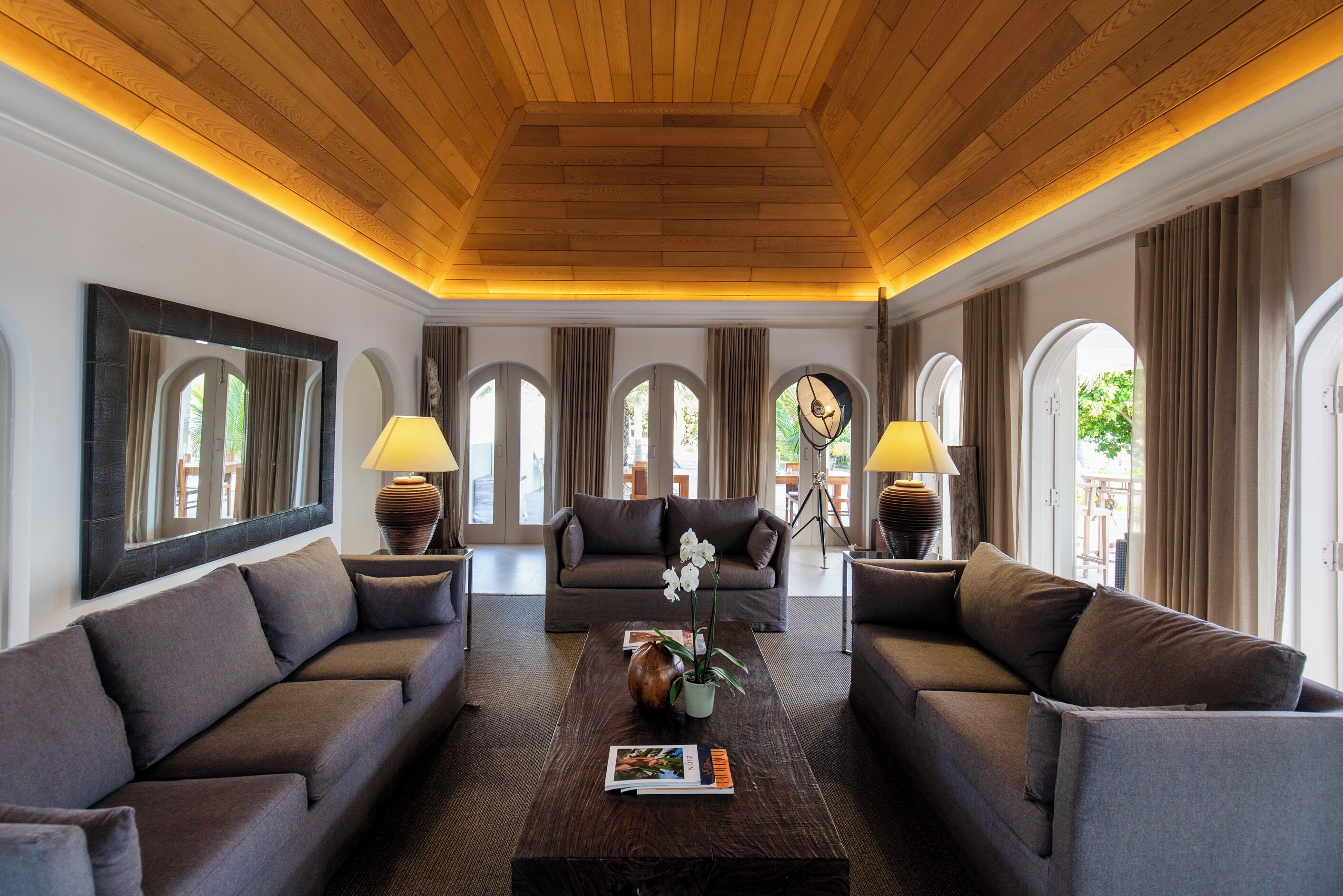 Un salón espacioso con techo de madera alto, dos sofás, una mesa de centro y un espejo grande.
