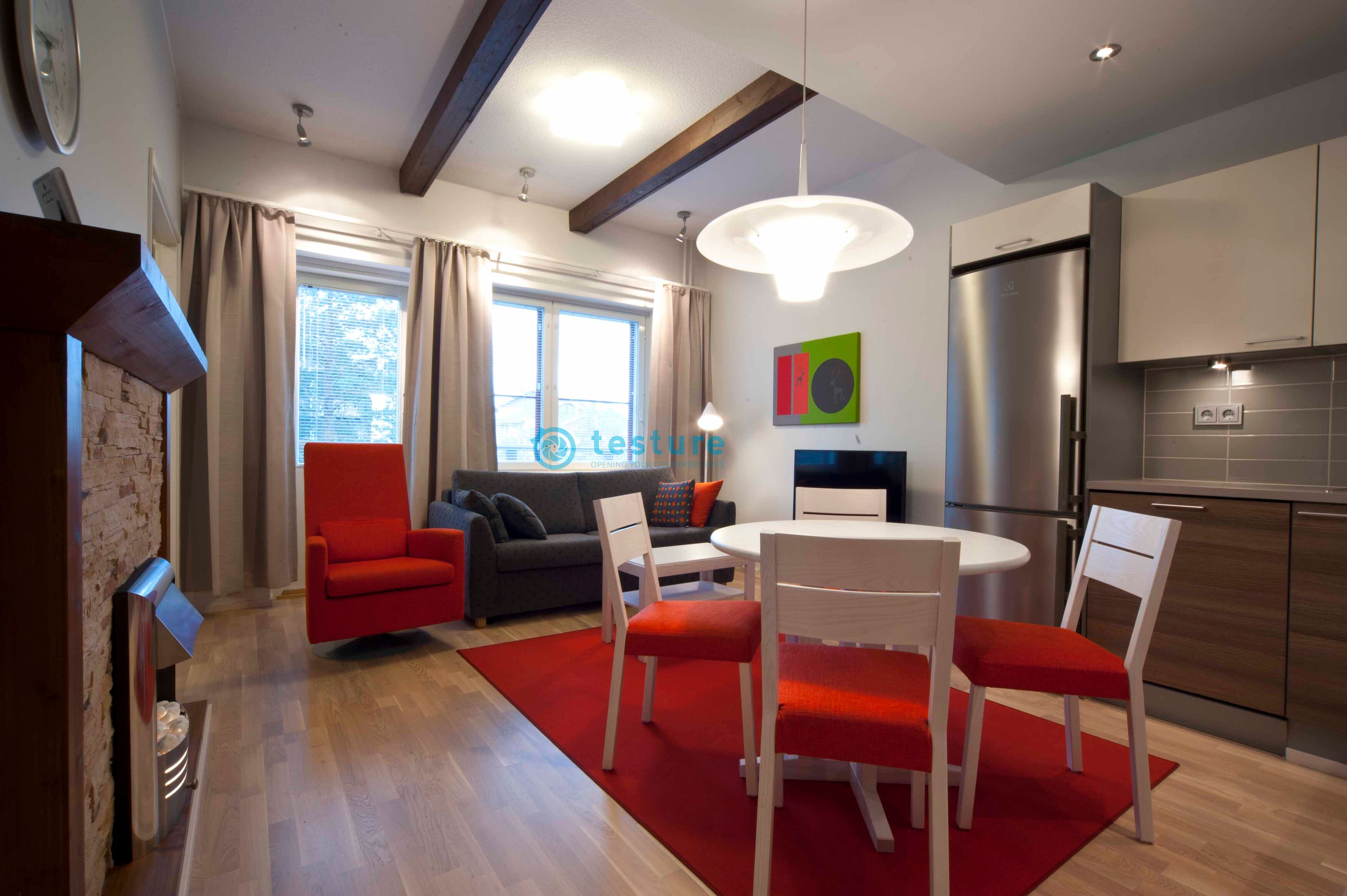 A modern kitchen with a built-in refrigerator, wooden cabinets, and a dining area with a red rug and white chairs.