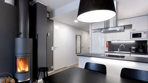 Una cocina moderna con estufa de leña integrada, un comedor con mesa y sillas, y una lámpara colgante grande.