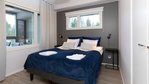 Un dormitorio moderno con una cama grande, una ventana con persianas, una mesita de noche con lámpara y vistas a árboles fuera.