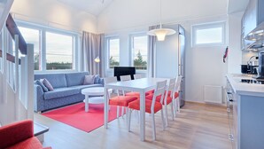 Una sala moderna con sofá, mesa de comedor y sillas, zona de cocina y ventanas amplias con vistas.