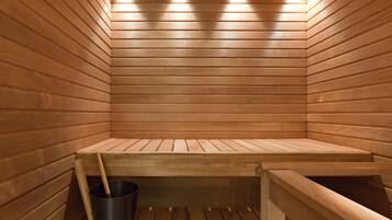A sauna with wooden walls and benches, a bucket, and a ceiling light fixture.