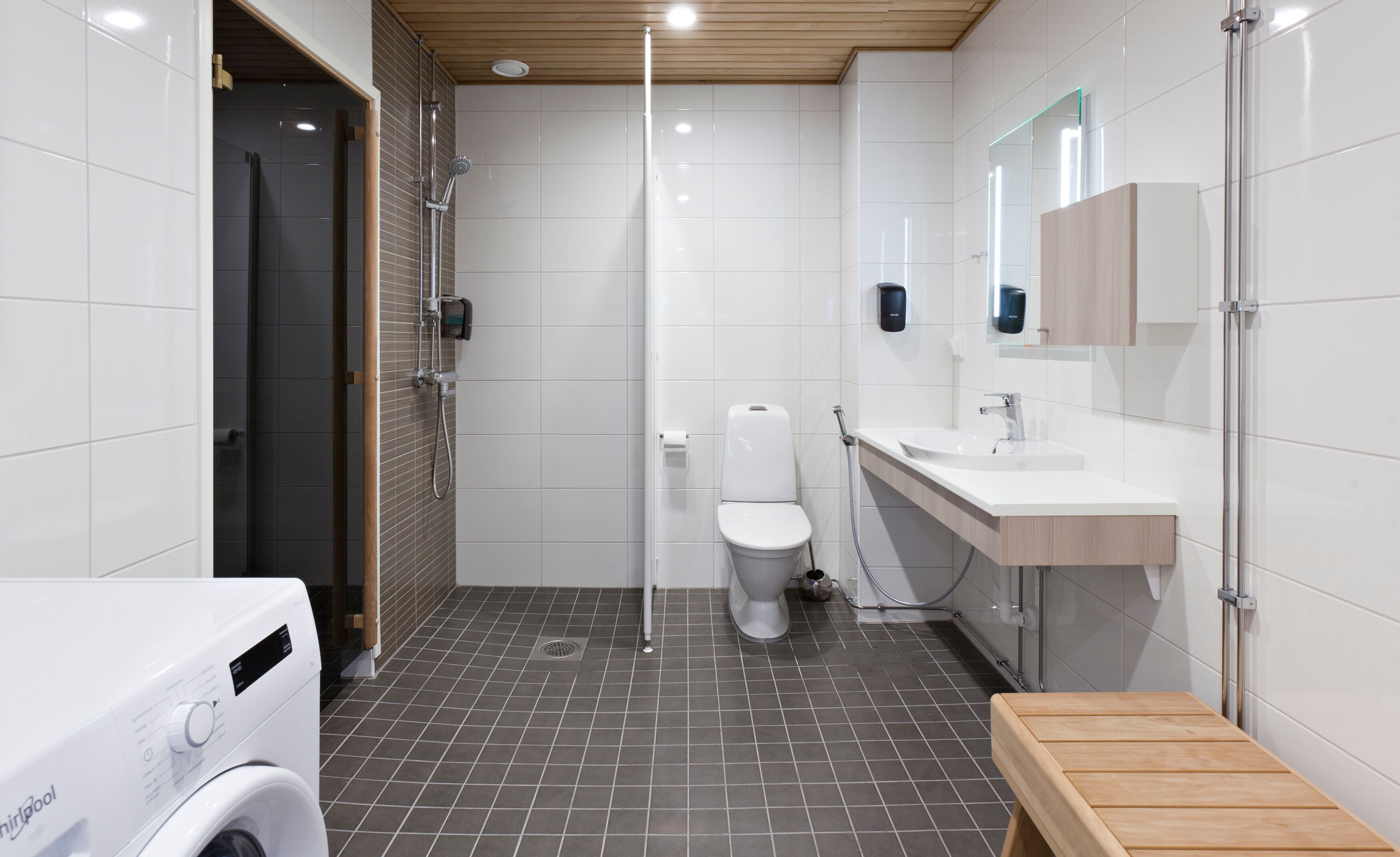 Ein modernes Badezimmer mit Dusche, Toilette, Waschbecken und einer hölzernen Sitzbank.