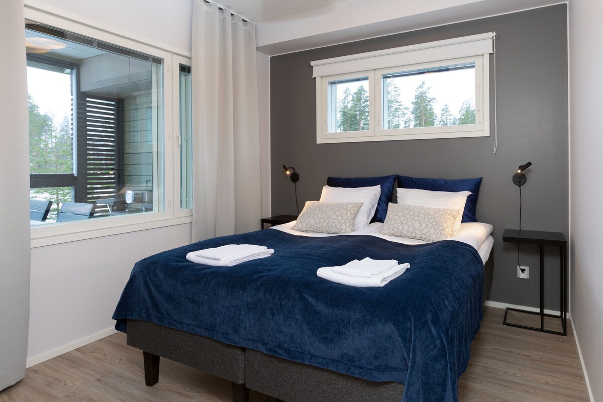 Un dormitorio moderno con una cama grande, una ventana, una mesita de noche y una lámpara de pared.