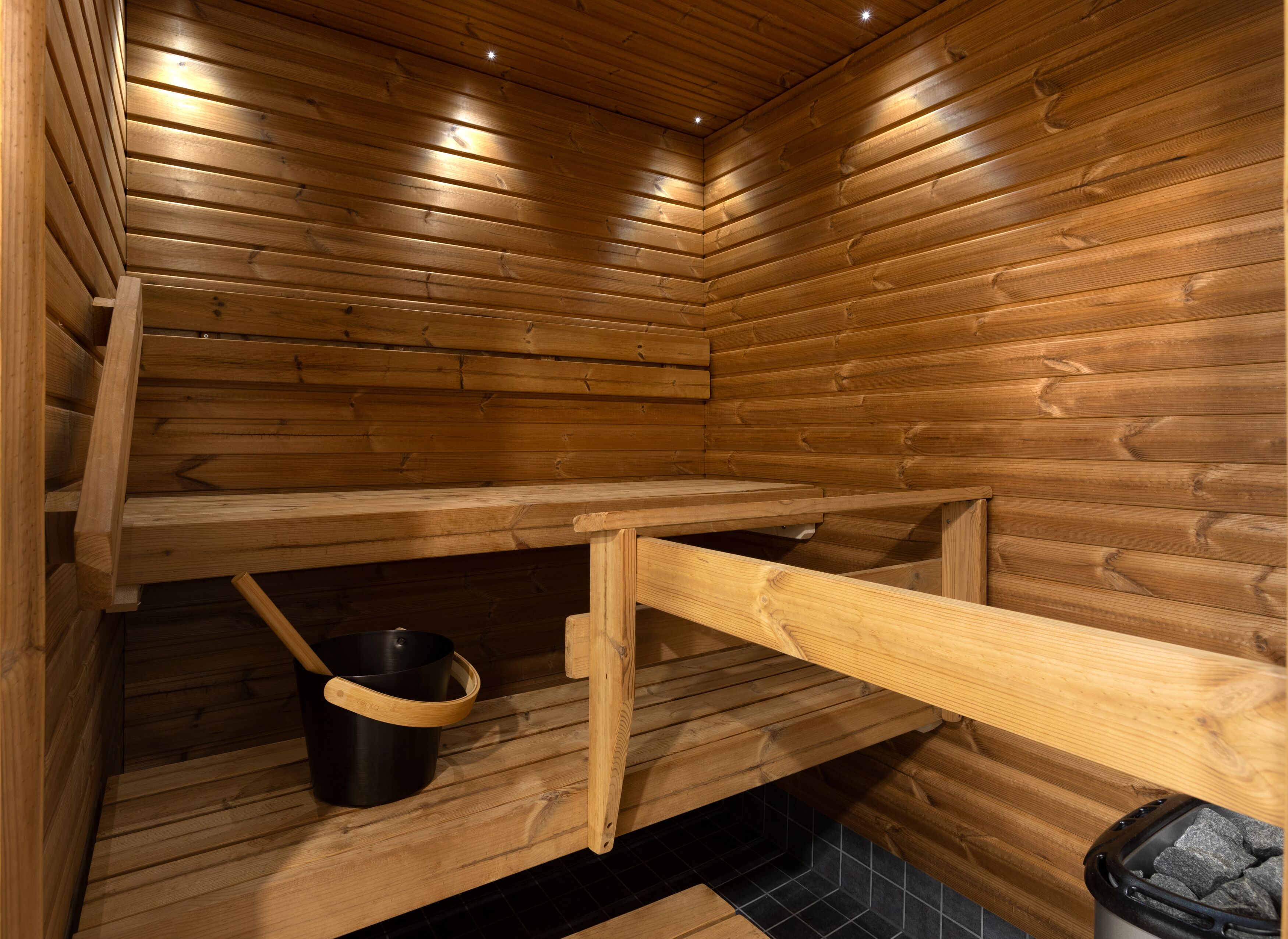 A wooden sauna with benches and a black trash bin.