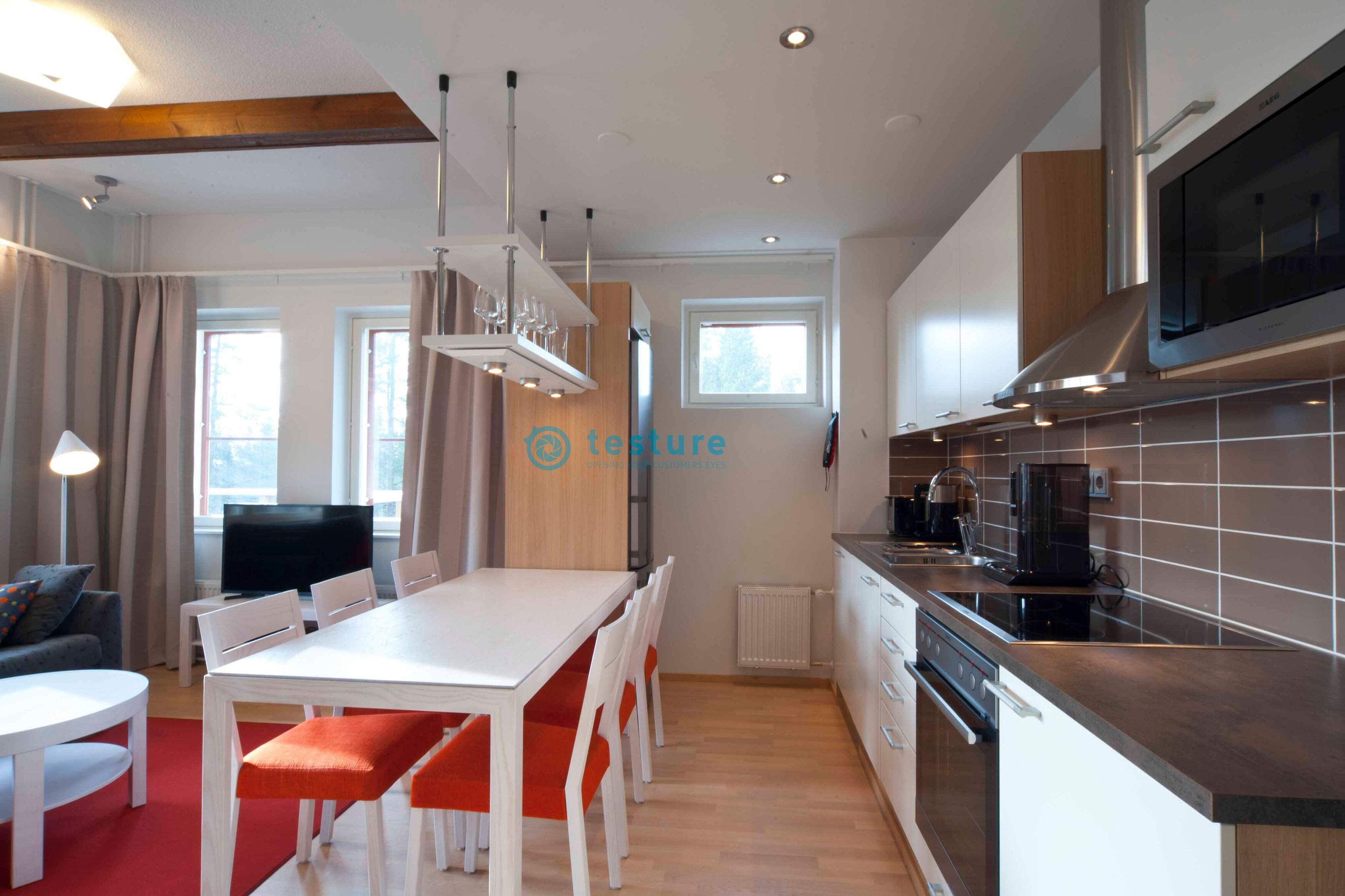 A modern kitchen with a built-in oven, microwave, and a large window. There is a dining area with a white table and orange chairs.