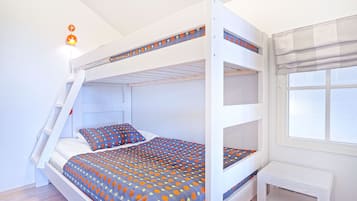 A bunk bed with a ladder, a small table, and a window with blinds.