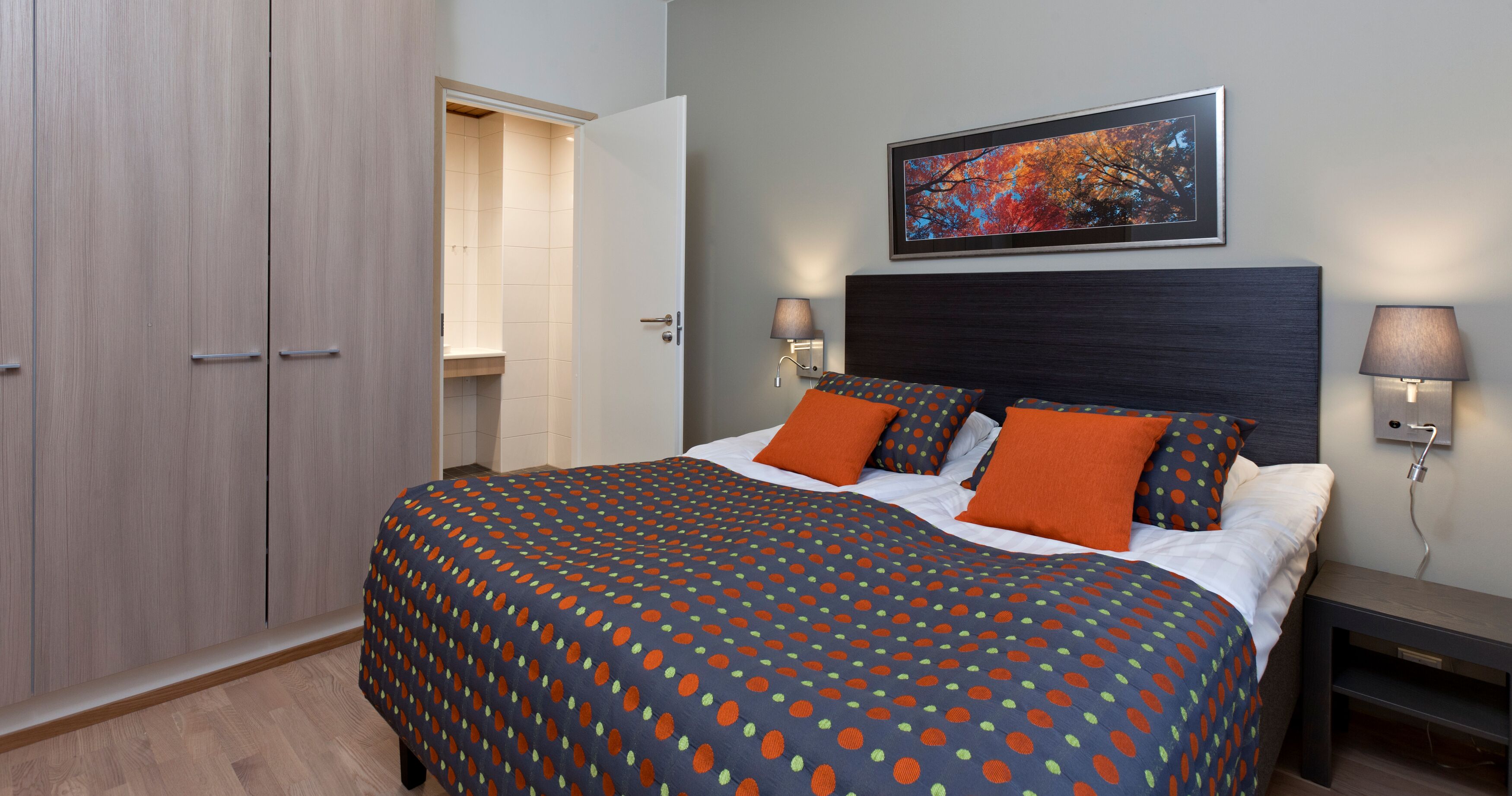A bedroom with a bed, two nightstands, a headboard, a wall-mounted painting, and a wardrobe.