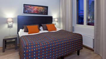 A neatly made bed with a polka dot bedspread, two side tables with lamps, a framed picture on the wall, and a window with curtains.