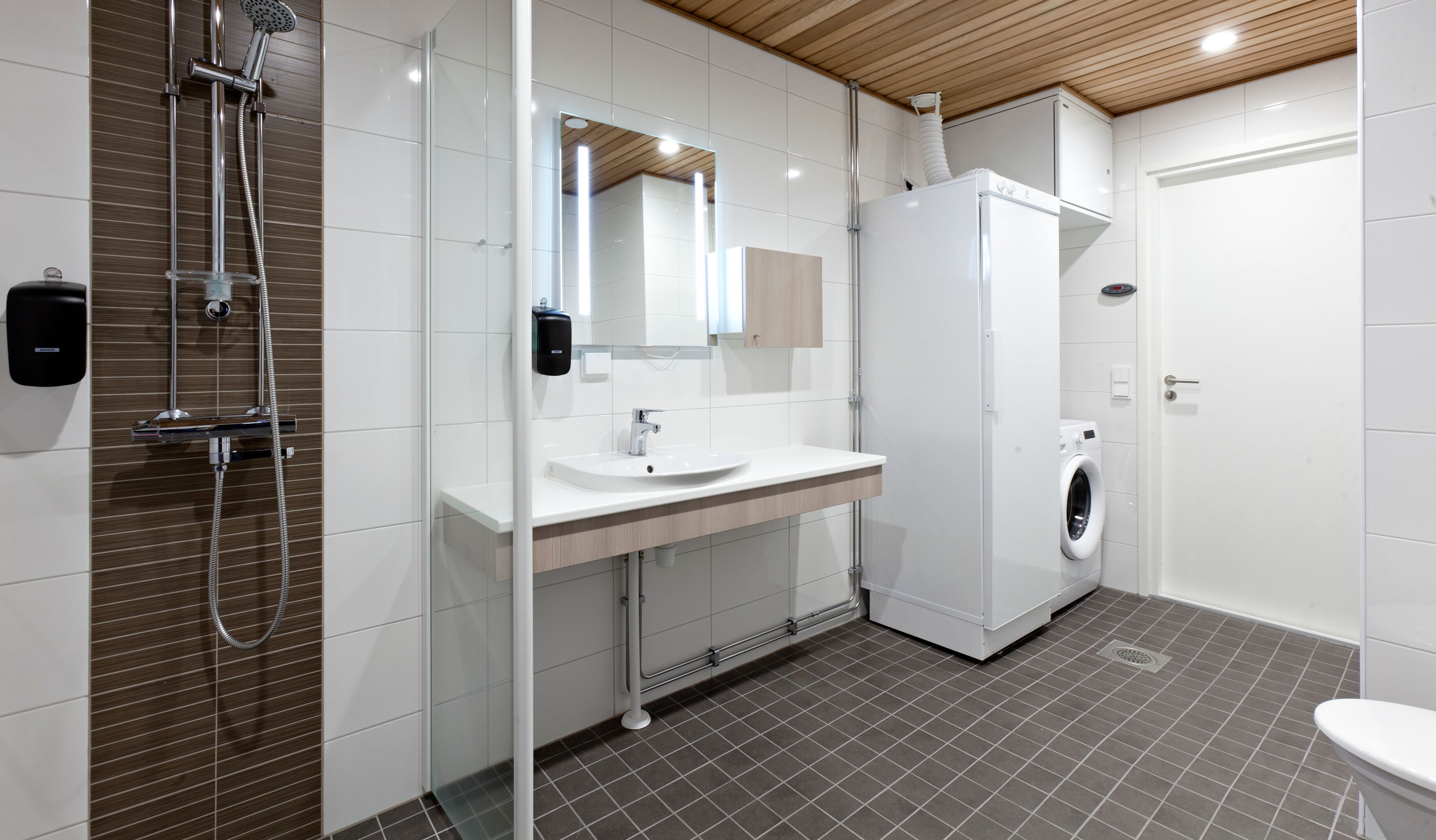 Une salle de bain moderne équipée d’une douche, d’un lavabo, d’un miroir et d’un lave-linge encastré.