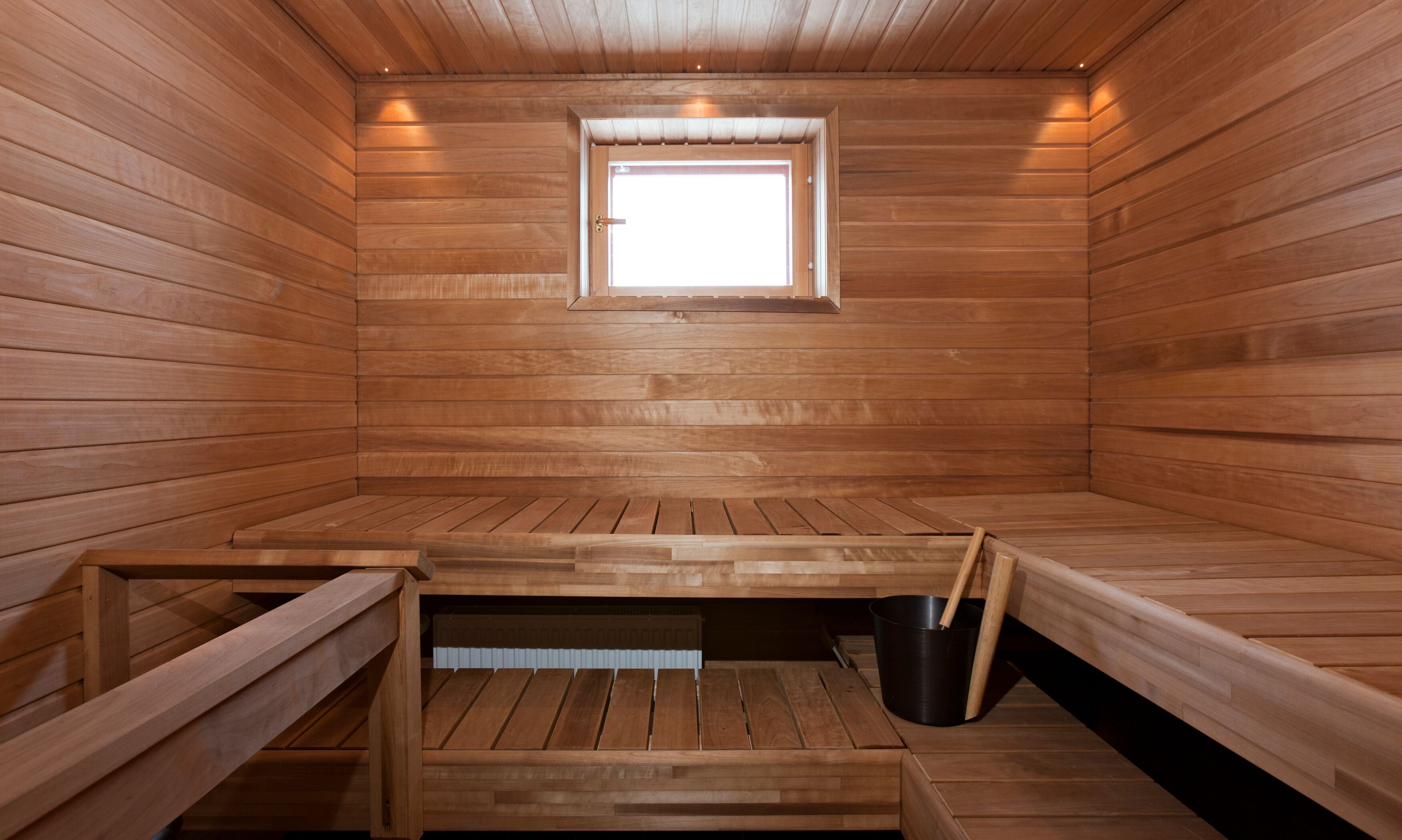 Een sauna met houten wanden, banken, een raam en een emmer.