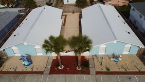 Un edificio de dos pisos con una alfombra roja que conduce a la entrada, rodeado de palmeras y un área de piscina decorativa con una escultura de tiburón.