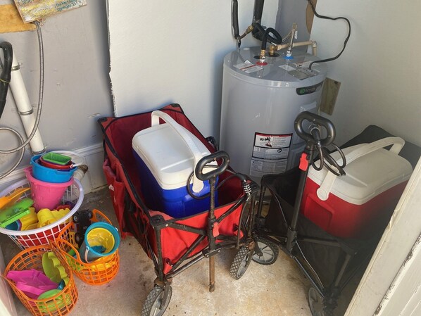 Un cuarto de servicio con un calentador de agua, un refrigerador rojo y diversos recipientes.
