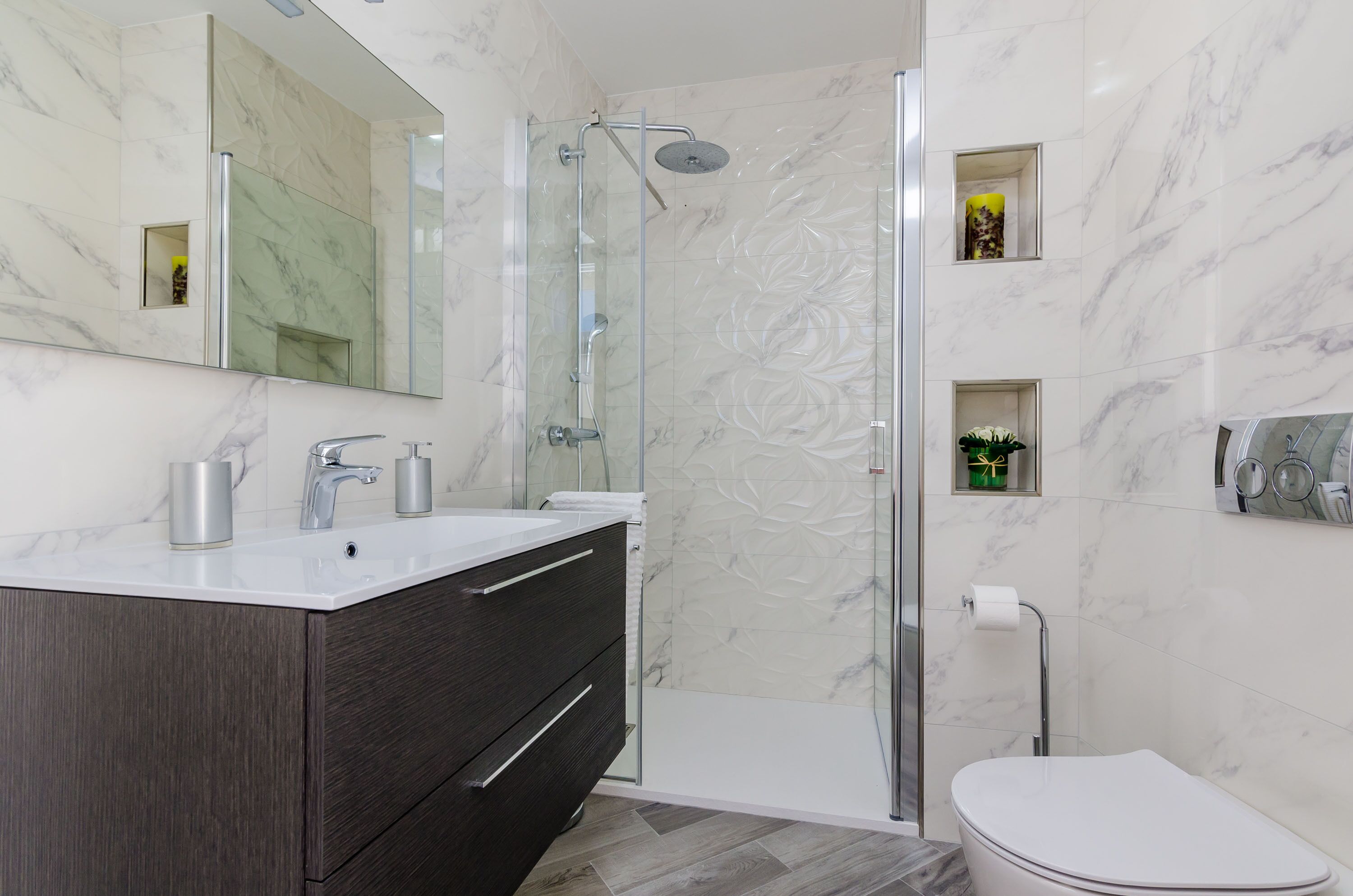 Une salle de bain moderne avec une douche à parois de verre, un lavabo blanc et un meuble sombre, ainsi que des toilettes.