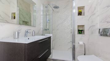 Une salle de bain moderne avec une douche à parois de verre, un lavabo blanc et un meuble sombre, ainsi que des toilettes.